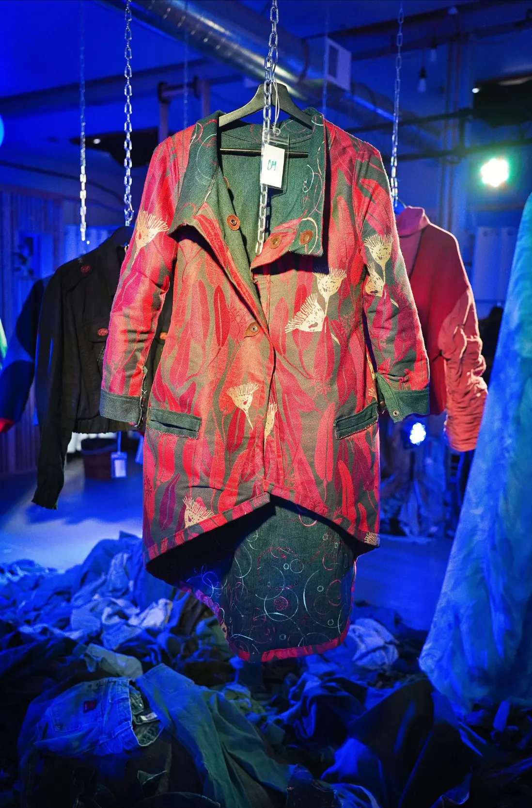 A red and green patterned coat displayed above reclaimed textiles